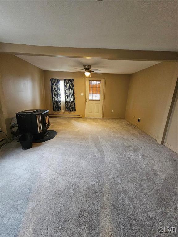 unfurnished living room with beamed ceiling, a wood stove, carpet flooring, ceiling fan, and a textured ceiling