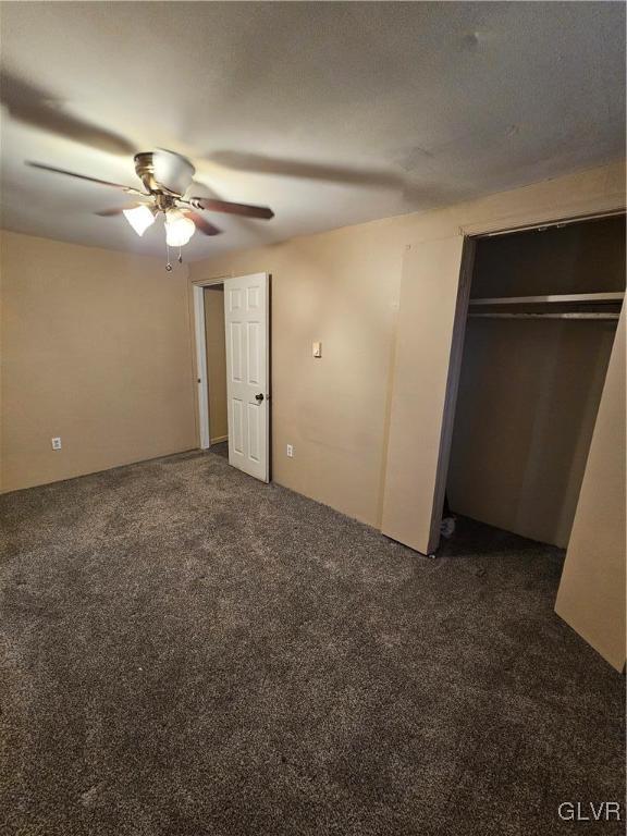 unfurnished bedroom with dark colored carpet, ceiling fan, and a closet