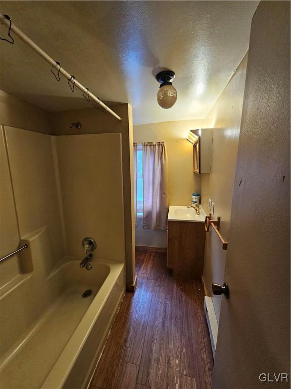 bathroom featuring a textured ceiling, shower / bathtub combination, vanity, hardwood / wood-style floors, and a baseboard heating unit