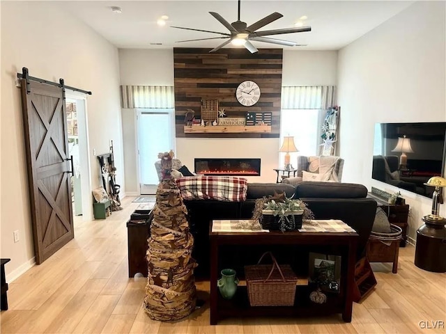 living room featuring wooden walls, a large fireplace, ceiling fan, a barn door, and light hardwood / wood-style flooring