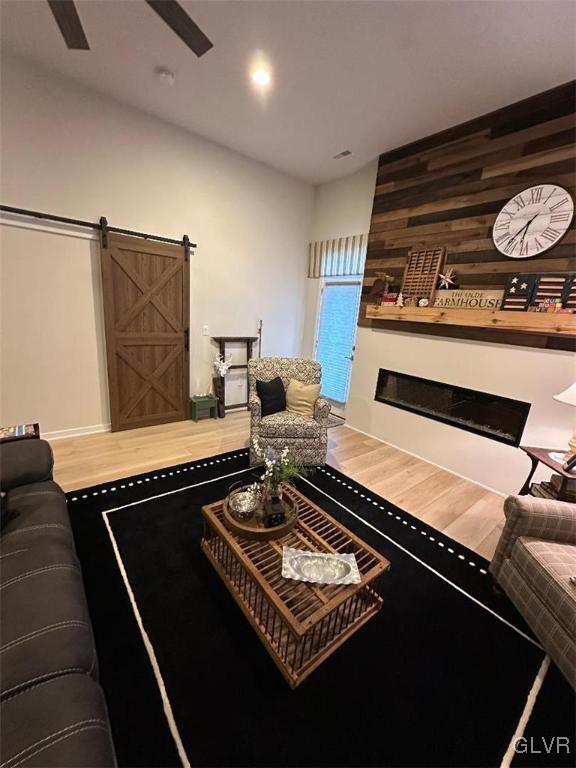 living room featuring wood-type flooring, a barn door, ceiling fan, and wood walls