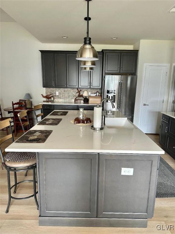 kitchen featuring pendant lighting, stainless steel fridge, a breakfast bar, a spacious island, and light stone counters