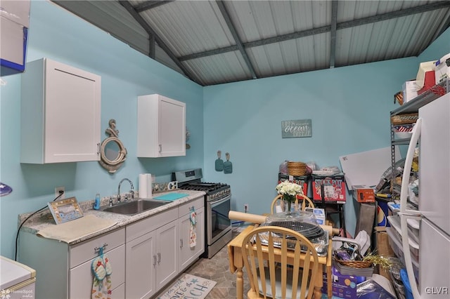 kitchen featuring vaulted ceiling, stainless steel gas range, sink, and white cabinets