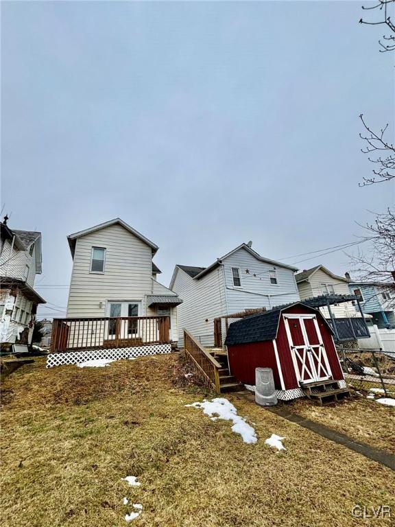 back of property with a lawn, a deck, and a storage shed