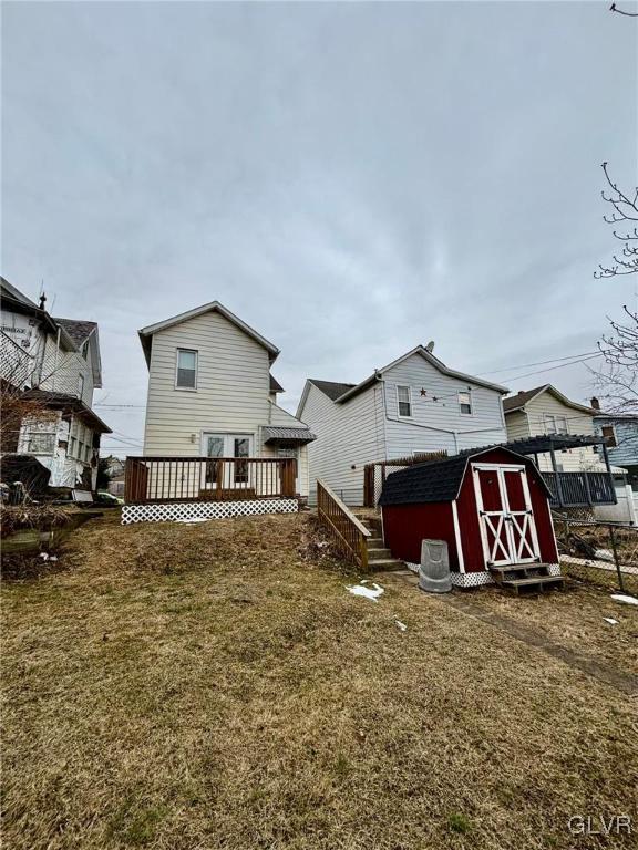 rear view of property featuring a yard, a deck, and a storage shed