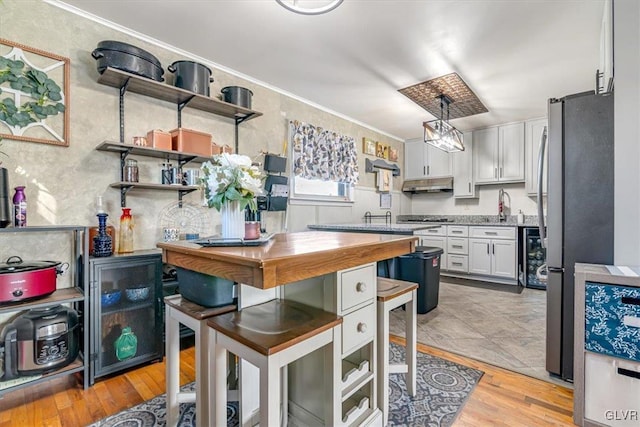 kitchen featuring white cabinetry, crown molding, decorative light fixtures, stainless steel fridge, and light hardwood / wood-style floors