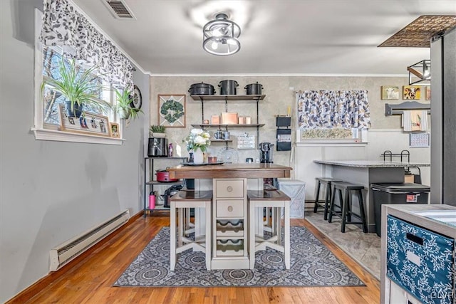 dining area featuring a baseboard radiator, ornamental molding, and light wood-type flooring