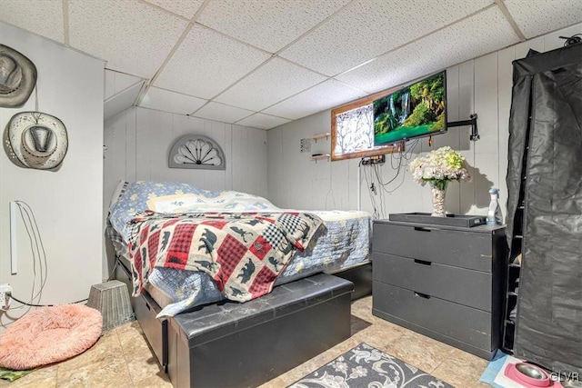 bedroom featuring a paneled ceiling and wooden walls