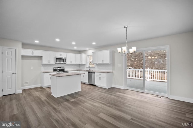 kitchen featuring a center island, hanging light fixtures, appliances with stainless steel finishes, white cabinets, and backsplash