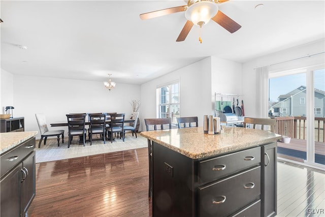 kitchen with a kitchen island, dark wood-type flooring, ceiling fan with notable chandelier, and light stone counters