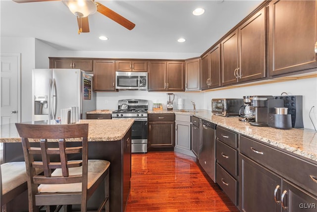 kitchen featuring appliances with stainless steel finishes, a breakfast bar, sink, light stone countertops, and dark wood-type flooring