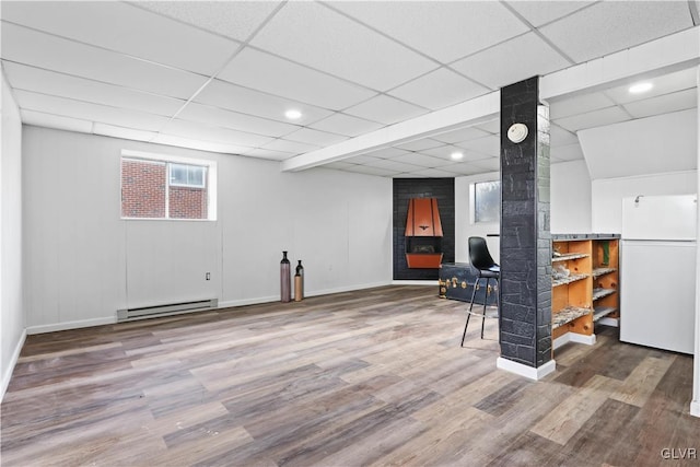 basement featuring white refrigerator, a paneled ceiling, wood-type flooring, and baseboard heating