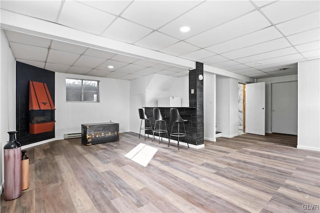 living room featuring a baseboard radiator, a paneled ceiling, wood-type flooring, and bar area