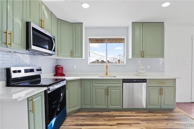 kitchen featuring sink, green cabinets, stainless steel appliances, light hardwood / wood-style floors, and backsplash