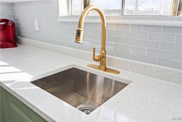 interior details featuring sink, green cabinets, light stone counters, and decorative backsplash