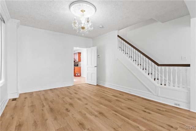 unfurnished living room with ornamental molding, a textured ceiling, a notable chandelier, and light hardwood / wood-style floors