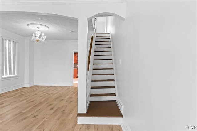 stairs with crown molding, a chandelier, hardwood / wood-style floors, and a textured ceiling