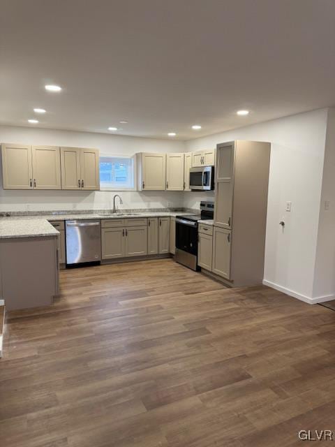 kitchen featuring stainless steel appliances, wood-type flooring, sink, and light stone counters