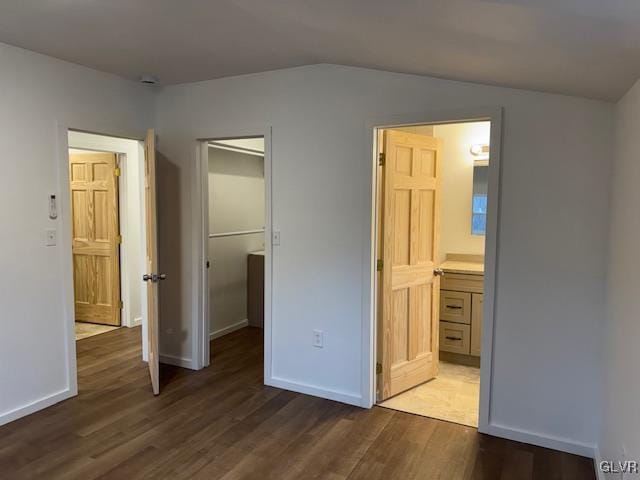 unfurnished bedroom featuring lofted ceiling, a spacious closet, dark hardwood / wood-style floors, and ensuite bathroom