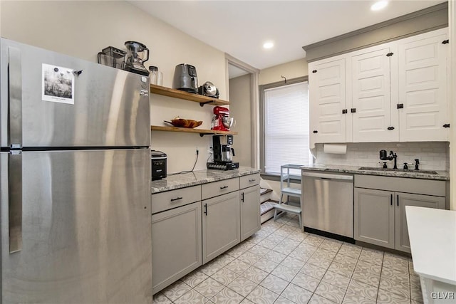 kitchen featuring sink, gray cabinetry, stainless steel appliances, light stone countertops, and decorative backsplash