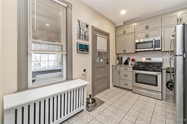 kitchen with backsplash, stainless steel appliances, radiator, and light tile patterned flooring