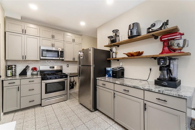 kitchen with tasteful backsplash, stainless steel appliances, light stone countertops, and light tile patterned floors