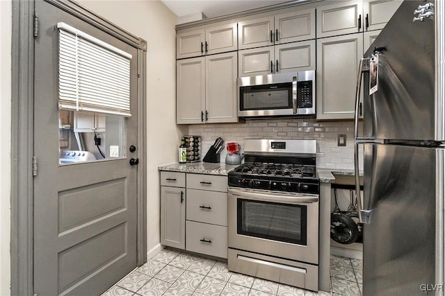 kitchen with light tile patterned floors, gray cabinets, appliances with stainless steel finishes, tasteful backsplash, and light stone countertops