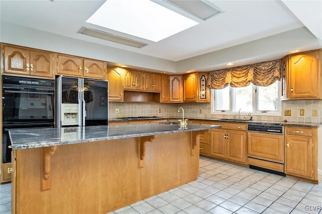 kitchen with sink, a breakfast bar, a center island with sink, and black appliances