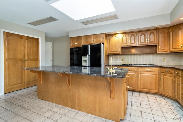 kitchen featuring sink, dark stone countertops, backsplash, a center island, and black appliances