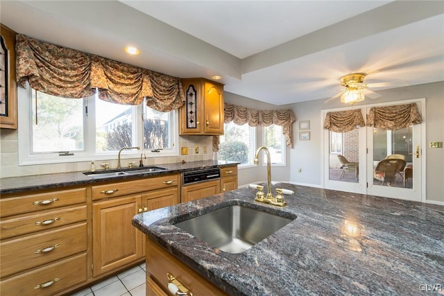 kitchen with sink, dark stone countertops, light tile patterned floors, and decorative backsplash