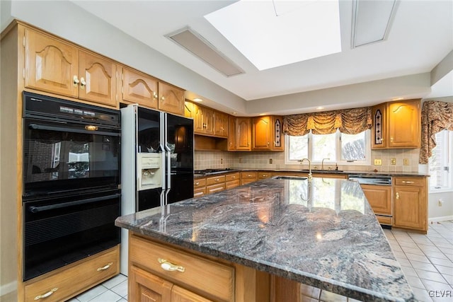 kitchen with tasteful backsplash, dark stone counters, a kitchen island with sink, and black appliances