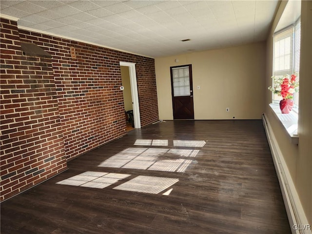 spare room featuring a baseboard radiator, brick wall, and dark hardwood / wood-style flooring