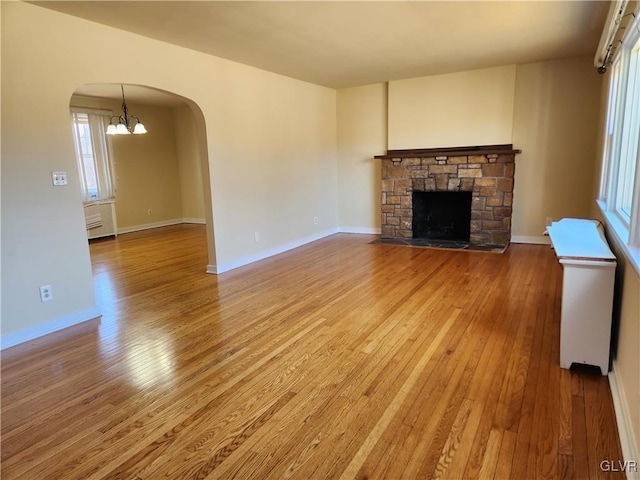 unfurnished living room featuring wood-type flooring, a stone fireplace, and a notable chandelier