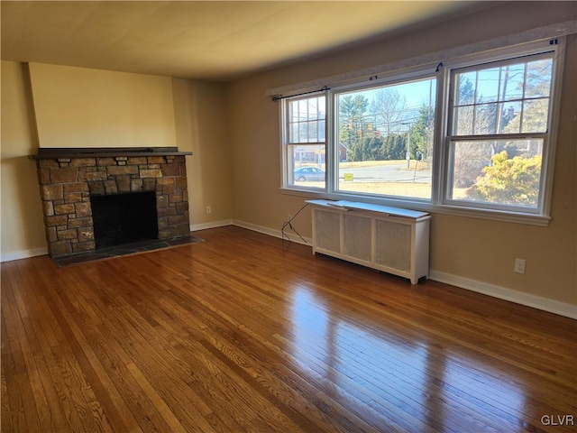 unfurnished living room featuring hardwood / wood-style flooring, a stone fireplace, and radiator