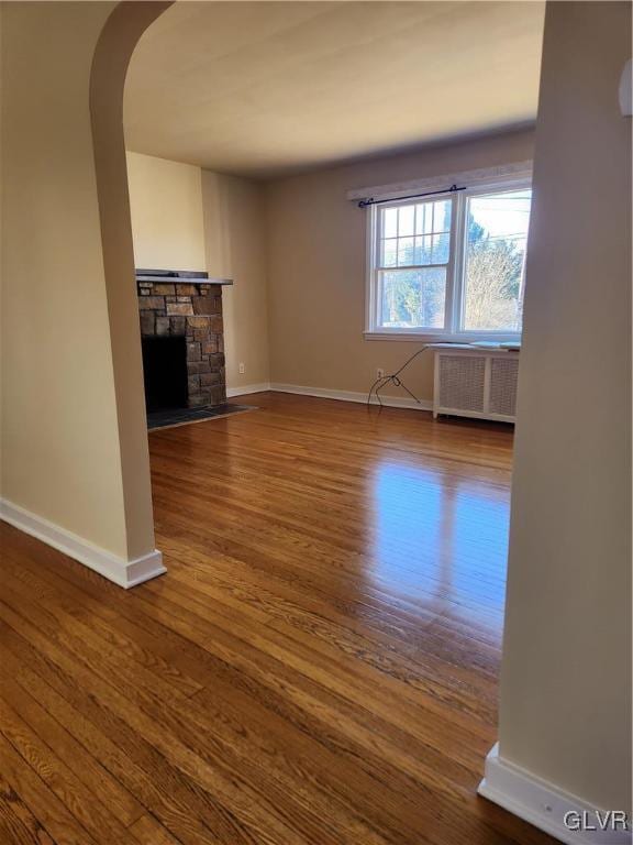 unfurnished living room featuring radiator heating unit, a fireplace, and wood-type flooring