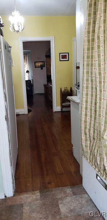 corridor with dark wood-type flooring and an inviting chandelier