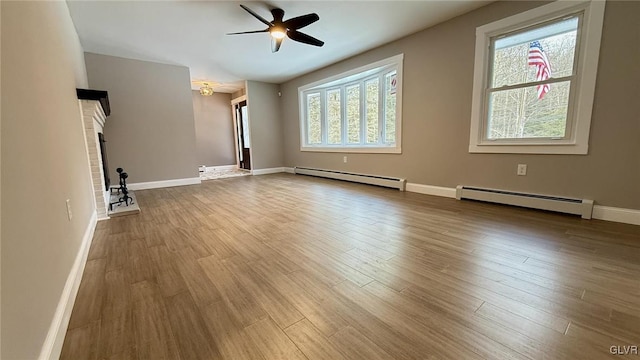 unfurnished living room featuring baseboard heating, ceiling fan, wood-type flooring, and a fireplace