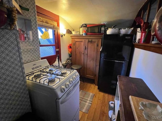 kitchen with black refrigerator, light hardwood / wood-style flooring, and white range with gas cooktop