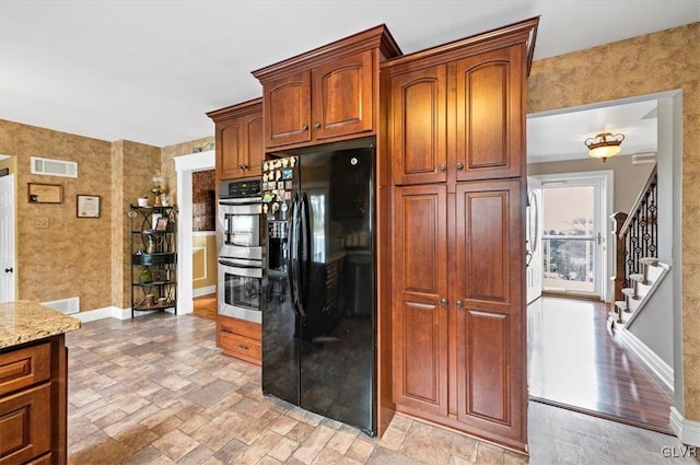 kitchen with black fridge, light stone counters, and double oven