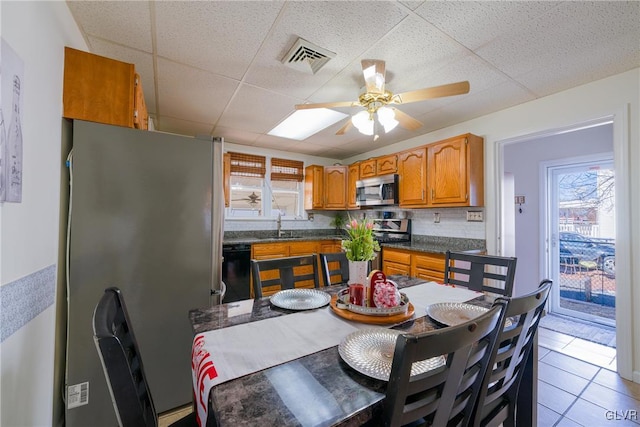 kitchen with light tile patterned floors, ceiling fan, appliances with stainless steel finishes, a drop ceiling, and decorative backsplash