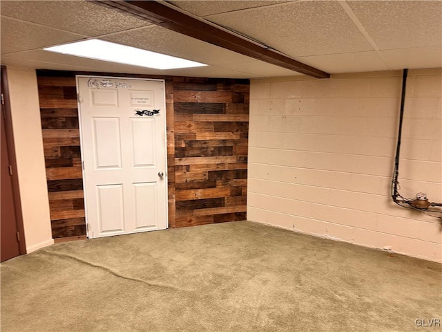 basement featuring carpet floors, a drop ceiling, and wood walls