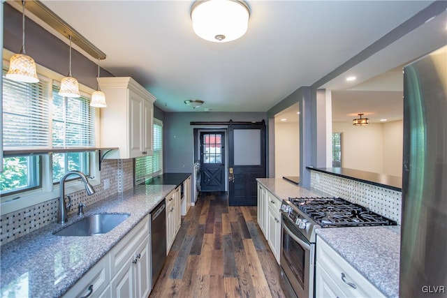 kitchen featuring appliances with stainless steel finishes, white cabinetry, sink, a barn door, and light stone countertops