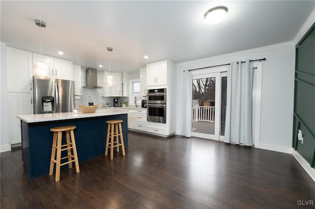 kitchen featuring white cabinetry, a center island, appliances with stainless steel finishes, pendant lighting, and wall chimney range hood