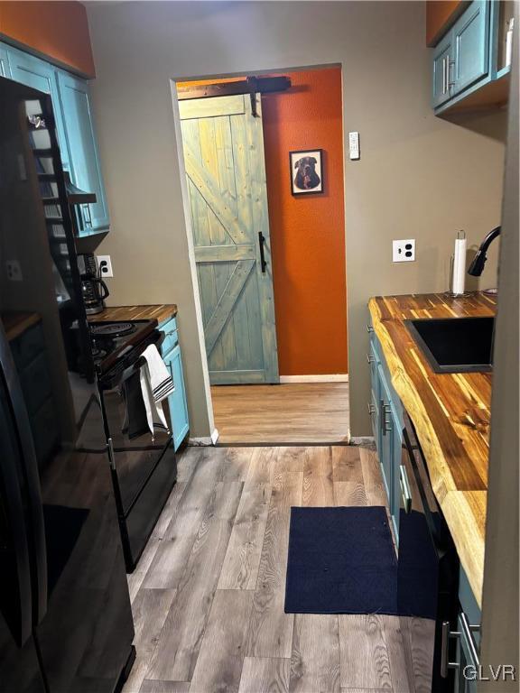 kitchen with wood counters, sink, black appliances, a barn door, and light hardwood / wood-style flooring