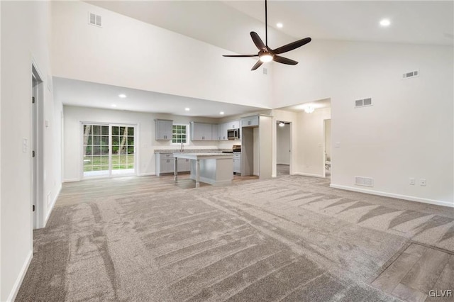 unfurnished living room with ceiling fan, light colored carpet, and high vaulted ceiling