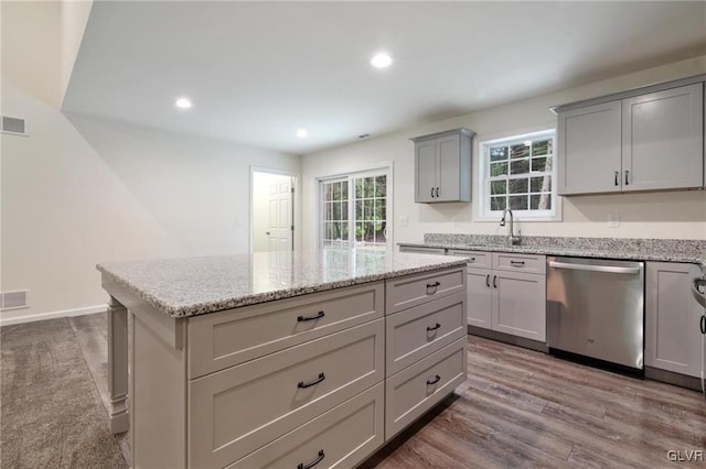 kitchen featuring hardwood / wood-style flooring, dishwasher, gray cabinetry, light stone countertops, and a kitchen island