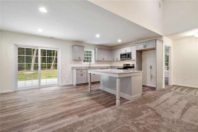 kitchen featuring a kitchen bar, a center island, appliances with stainless steel finishes, gray cabinets, and light stone countertops