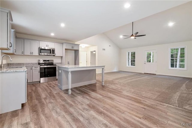 kitchen with light stone countertops, appliances with stainless steel finishes, a center island, and sink