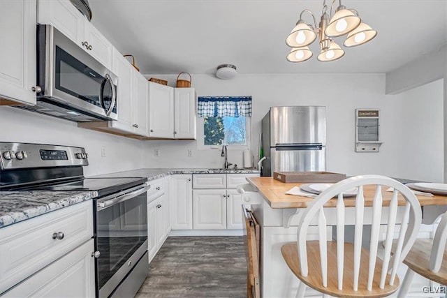 kitchen featuring white cabinetry, light stone counters, hanging light fixtures, dark hardwood / wood-style flooring, and stainless steel appliances