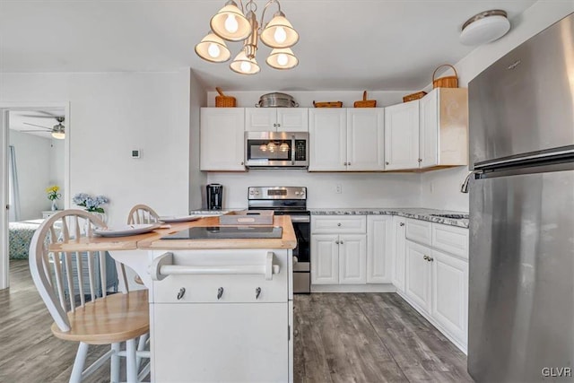 kitchen with appliances with stainless steel finishes, hardwood / wood-style floors, white cabinets, a kitchen bar, and hanging light fixtures